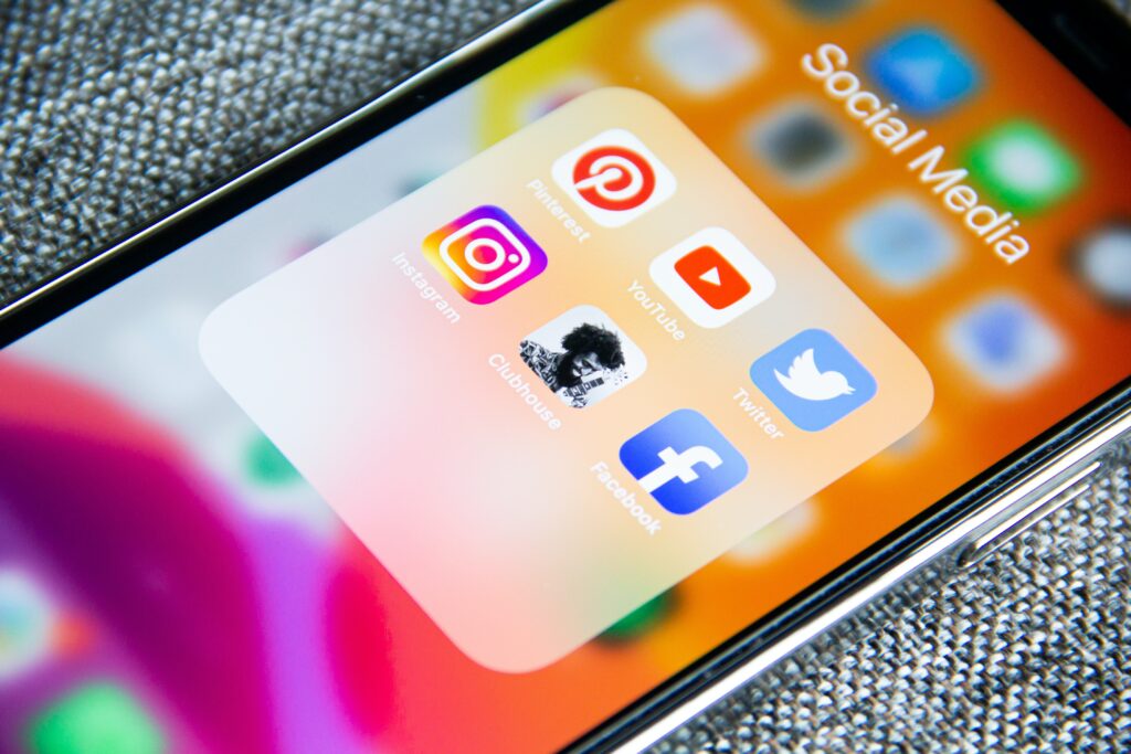 A smartphone close-up displays a folder of social media icons, including Pinterest, YouTube, Twitter, Instagram, and Facebook.