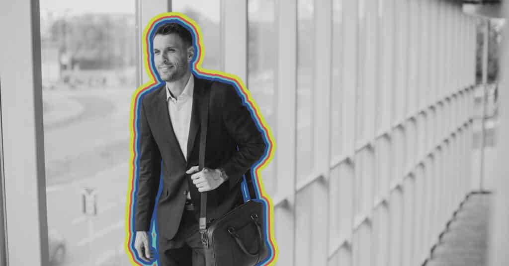 A businessman walks down a well lit corridor with a briefcase, in black and white accented by rainbow lines.