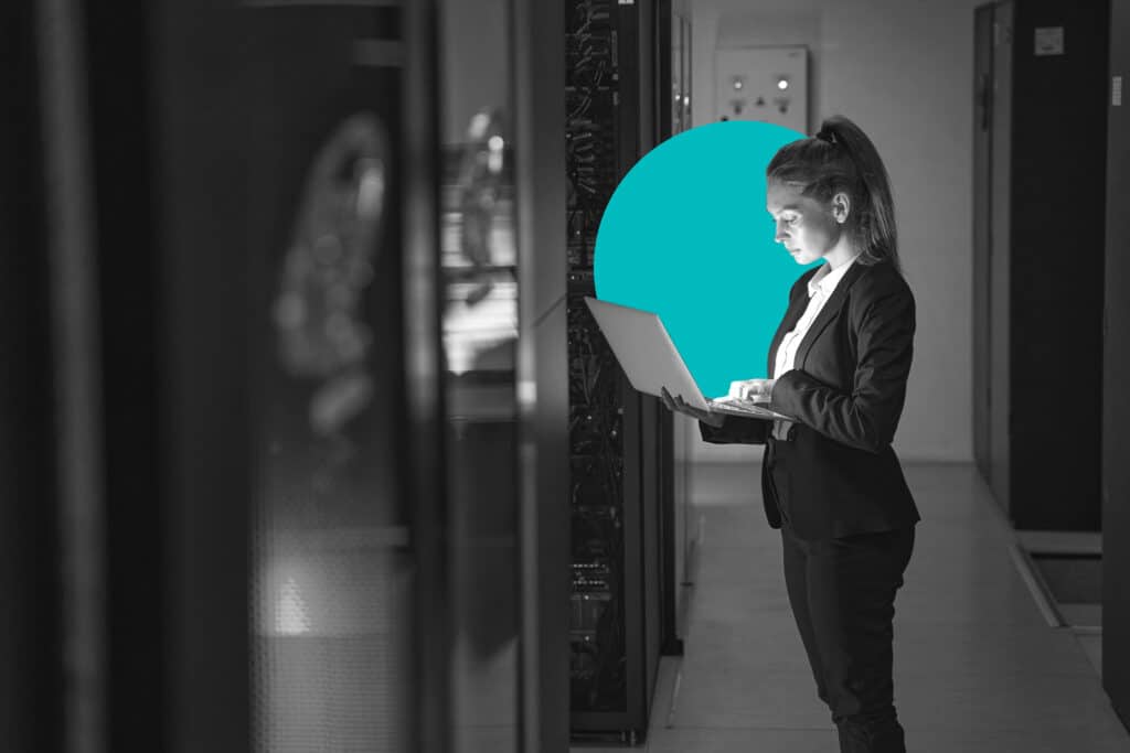 A woman in a data center holds up a laptop and probably clicks a cta on her trackpad.