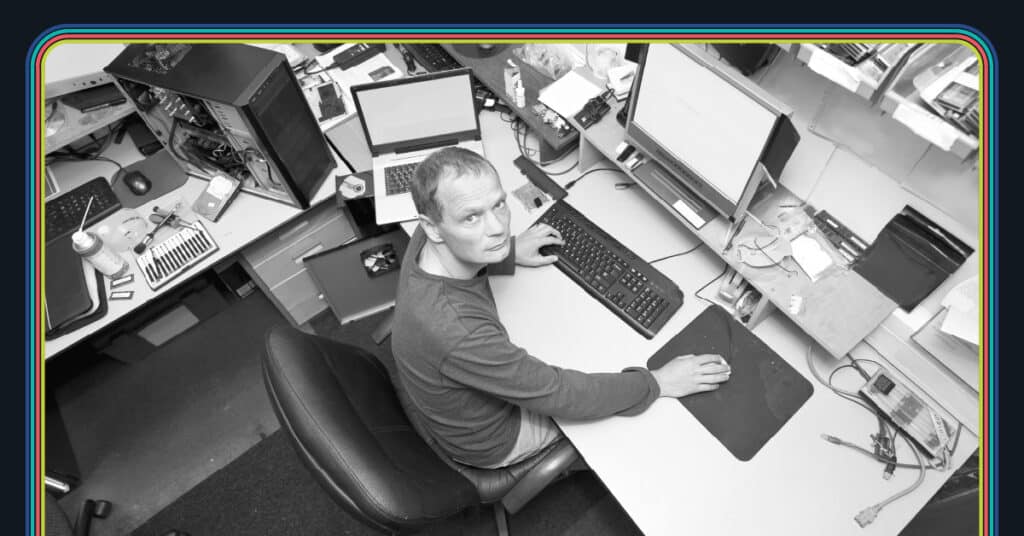 A miserable looking engineer looks up at the camera, surrounded by computers and broken equipment, in the midst of a marketing automation migration.