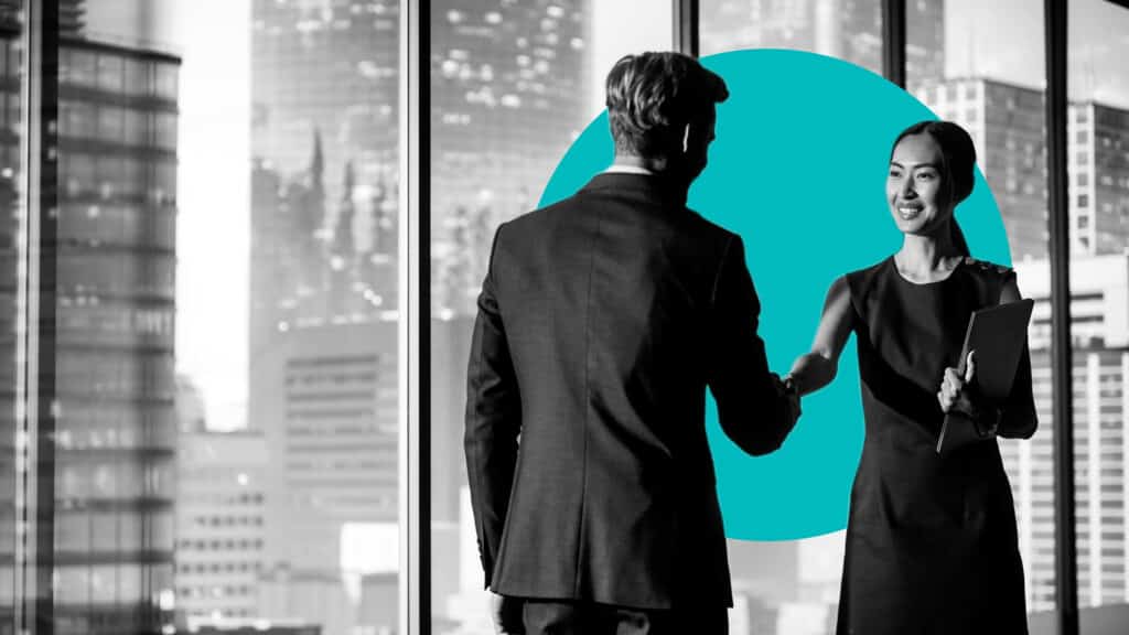 An asian woman and man in business attire shake hands in an urban setting.