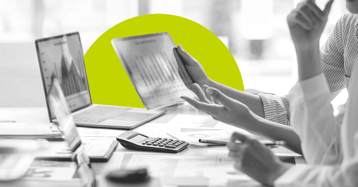 Multiple devices, documents and work collected on a conference table with multiple people visibly collaborating.